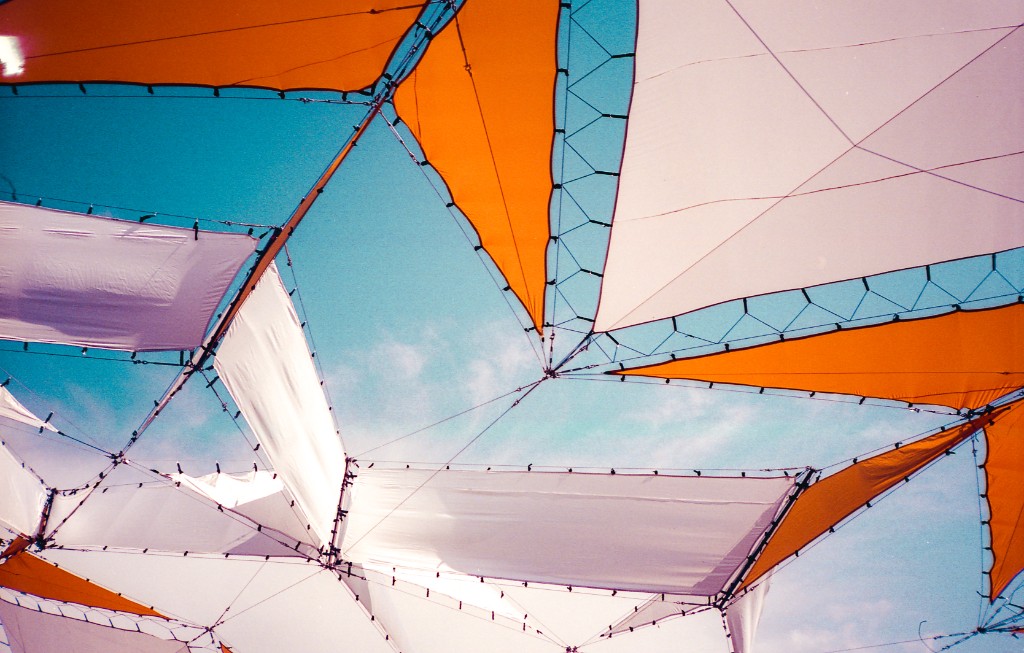 Looking up at orange and white fabric canopy panels stretched across a bright blue sky.