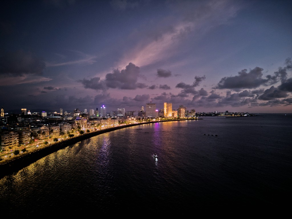 Coastal city skyline at dusk with a curved boulevard of lights along the waterfront.