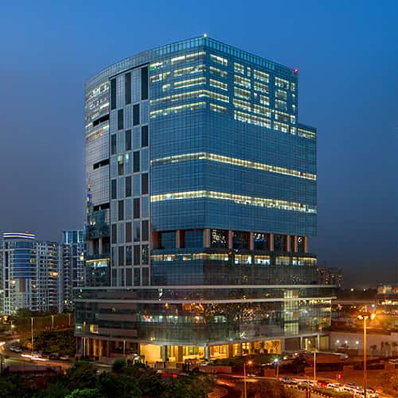 Modern glass office tower lit at night against a deep blue twilight sky.